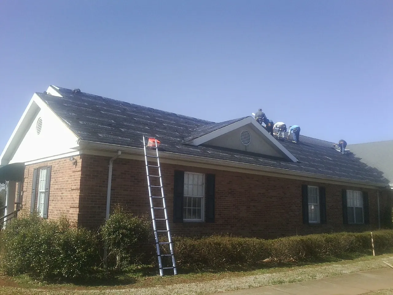 Crew tearing shingles off a brick ranch roof with a ladder set — Emergency Roof Repair work by our crew in Shelley
