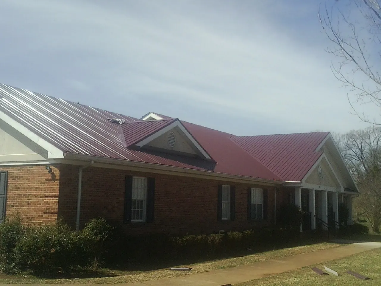 Red metal roof with gabled entries on a long brick building, from a Hail Damage Roof Repair job in Shelley