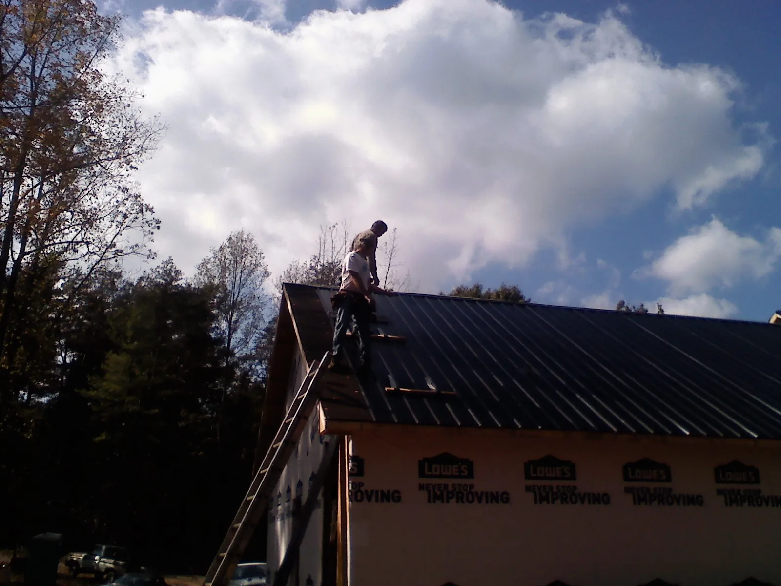 Roofer fastening dark metal panels high against a cloudy sky, from a Roof Inspection job in Shelley