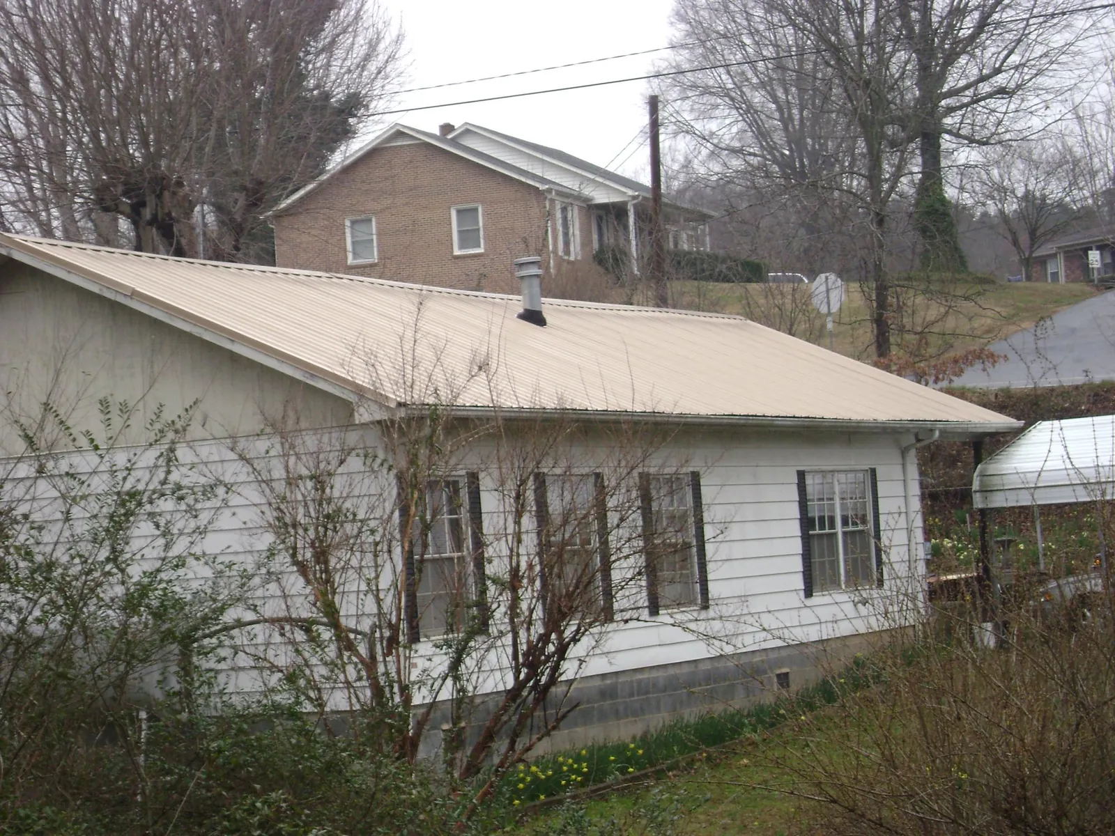 Tan metal roof on a white sided house set into a hillside — Commercial Roofing by Roofing Brothers in Shelley